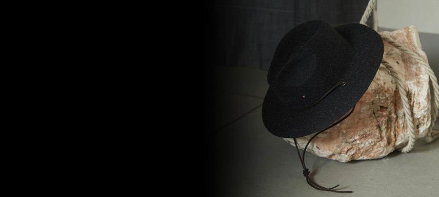 Black felt Italian hat with chin strap, displayed on a stone with rope in natural light
