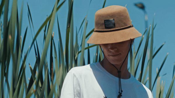 Man wearing a tan felt bucket hat with chin strap outdoors among tall grass