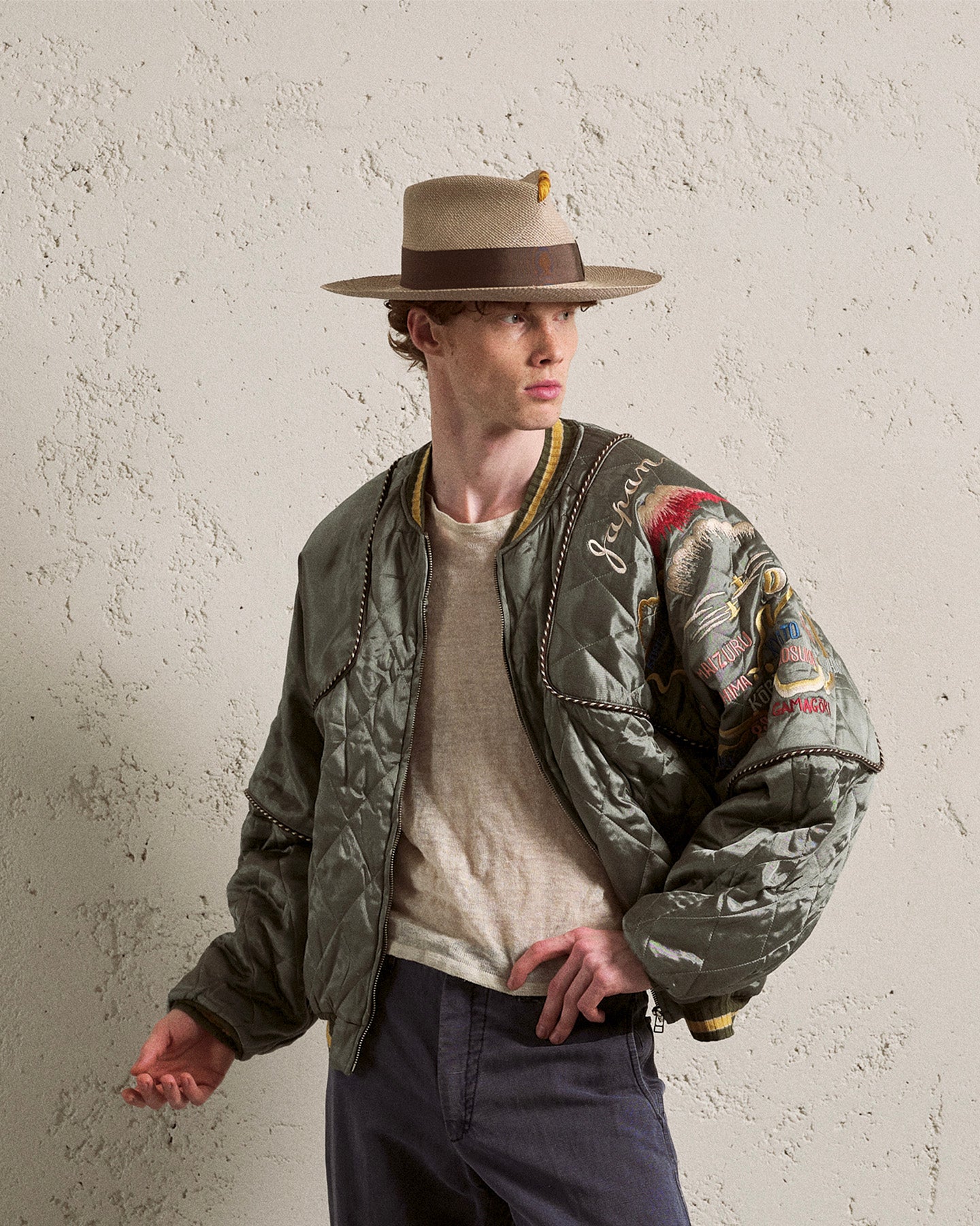 Man wearing a wide-brim straw hat with brown band and olive quilted bomber jacket