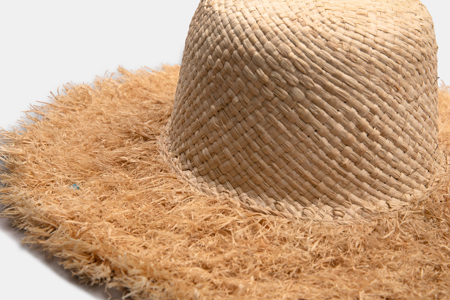 Close-up of a handmade wide brim straw hat with a frayed edge on a plain background