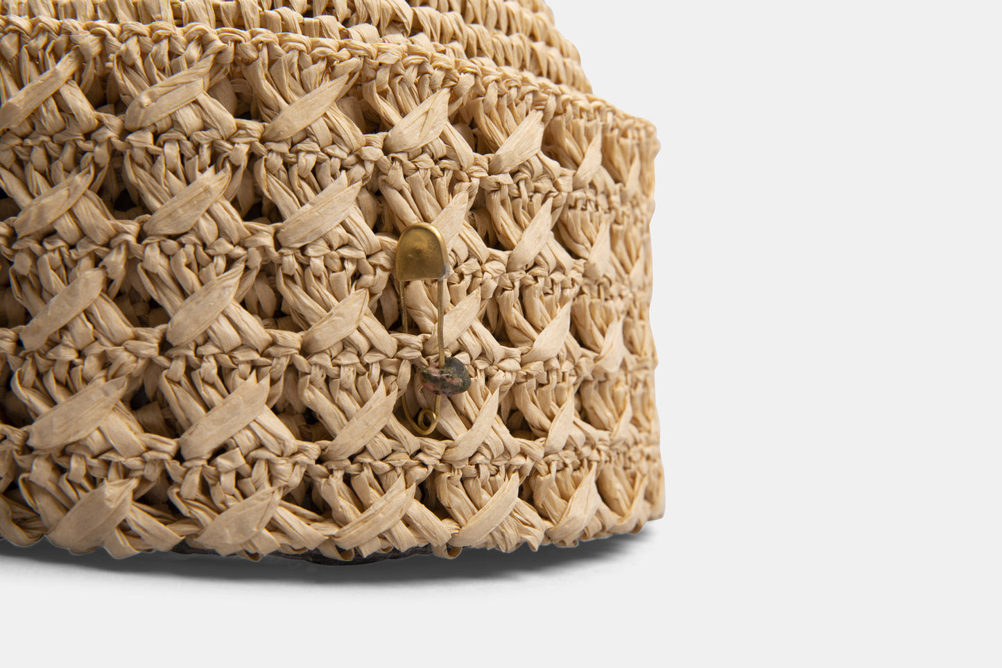 Close-up of woven straw hat with wide braid and decorative metal pin detail.