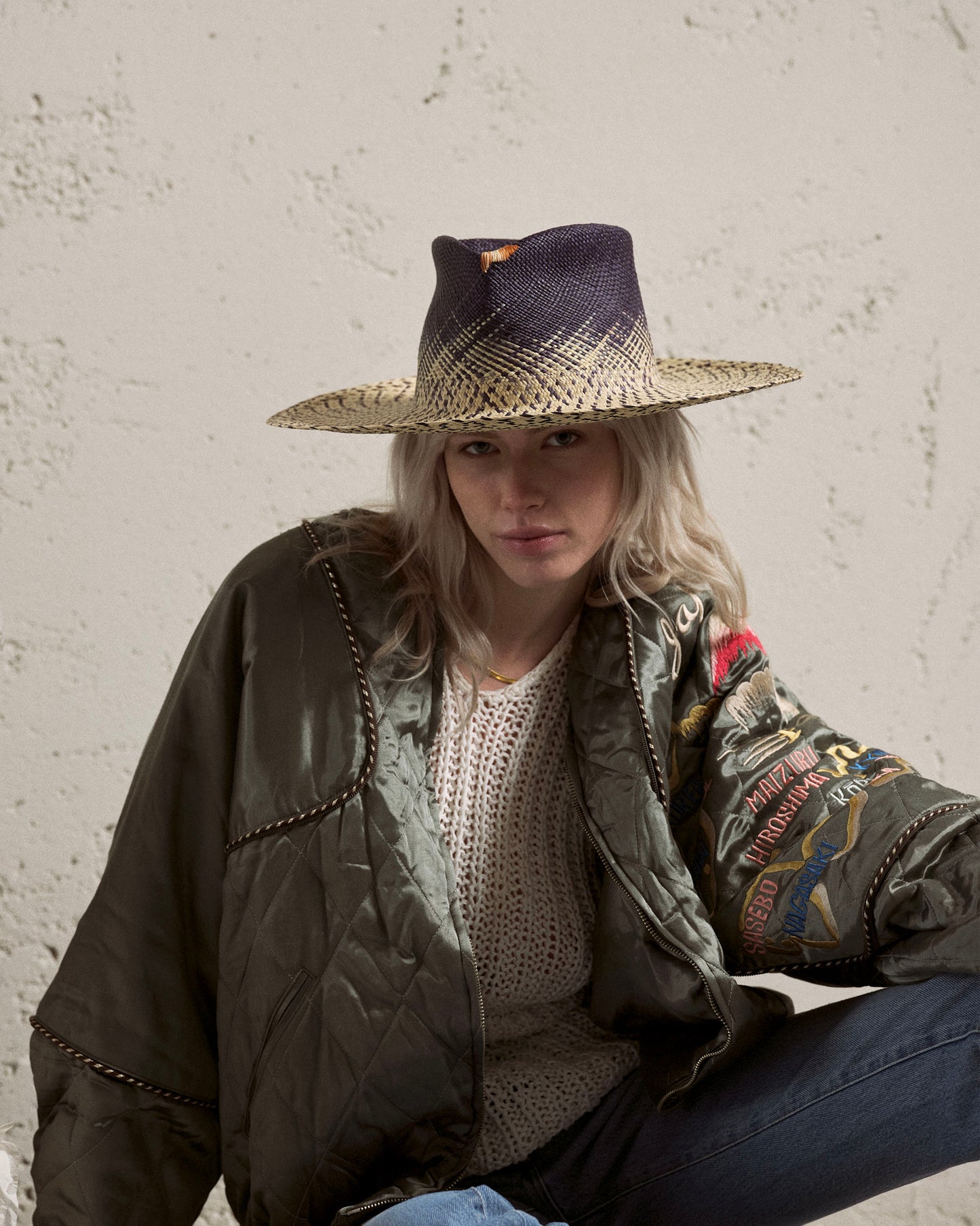 Woman wearing a wide-brim blue and straw Panama hat and quilted green jacket indoors