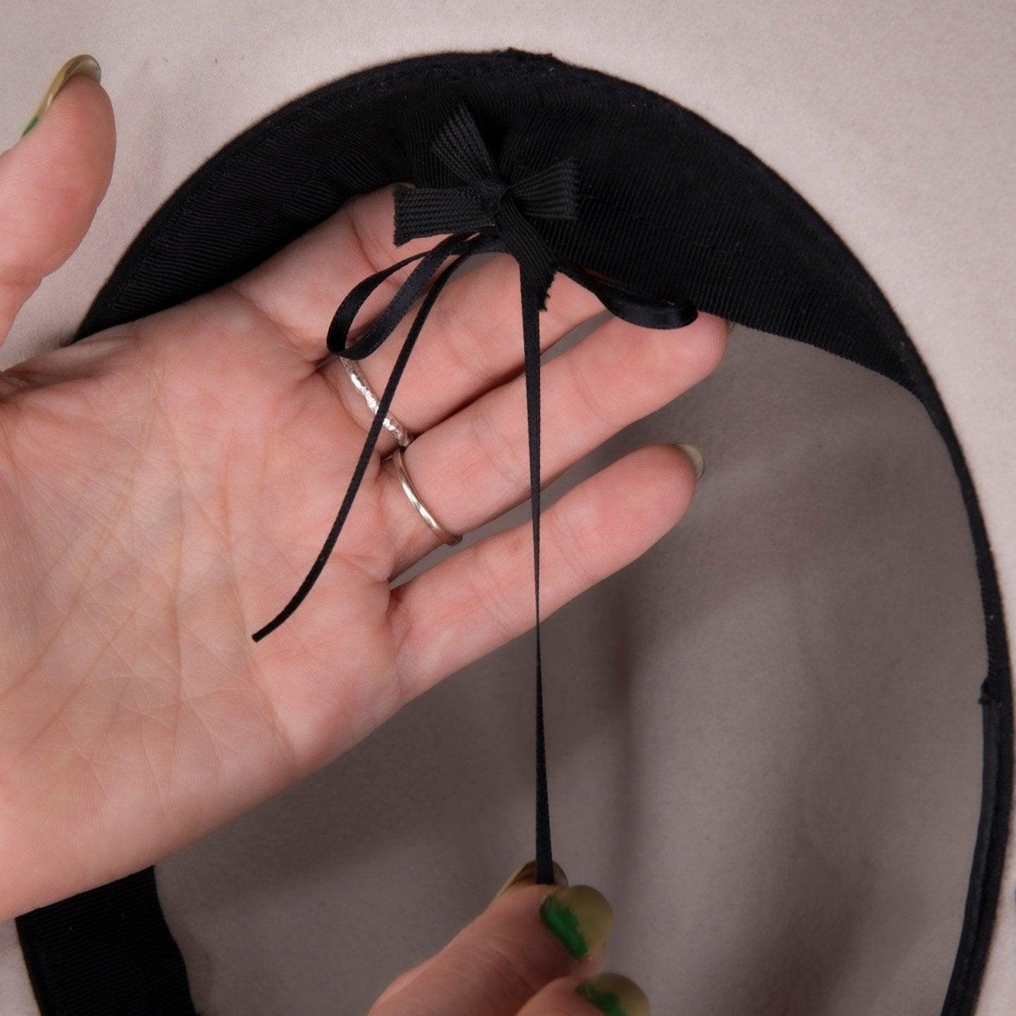 Hand adjusting inner ribbon of a beige felt hat with black band for custom fit