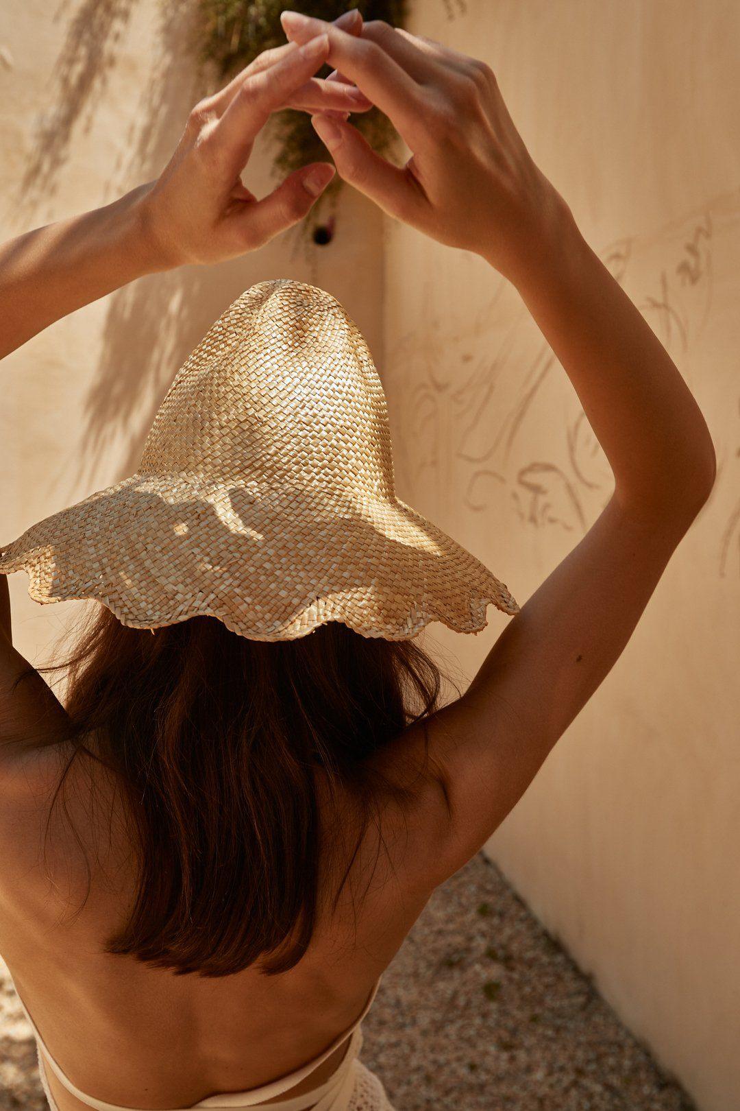 Woman in summer sunlight wearing wide-brimmed woven straw hat with wavy edge