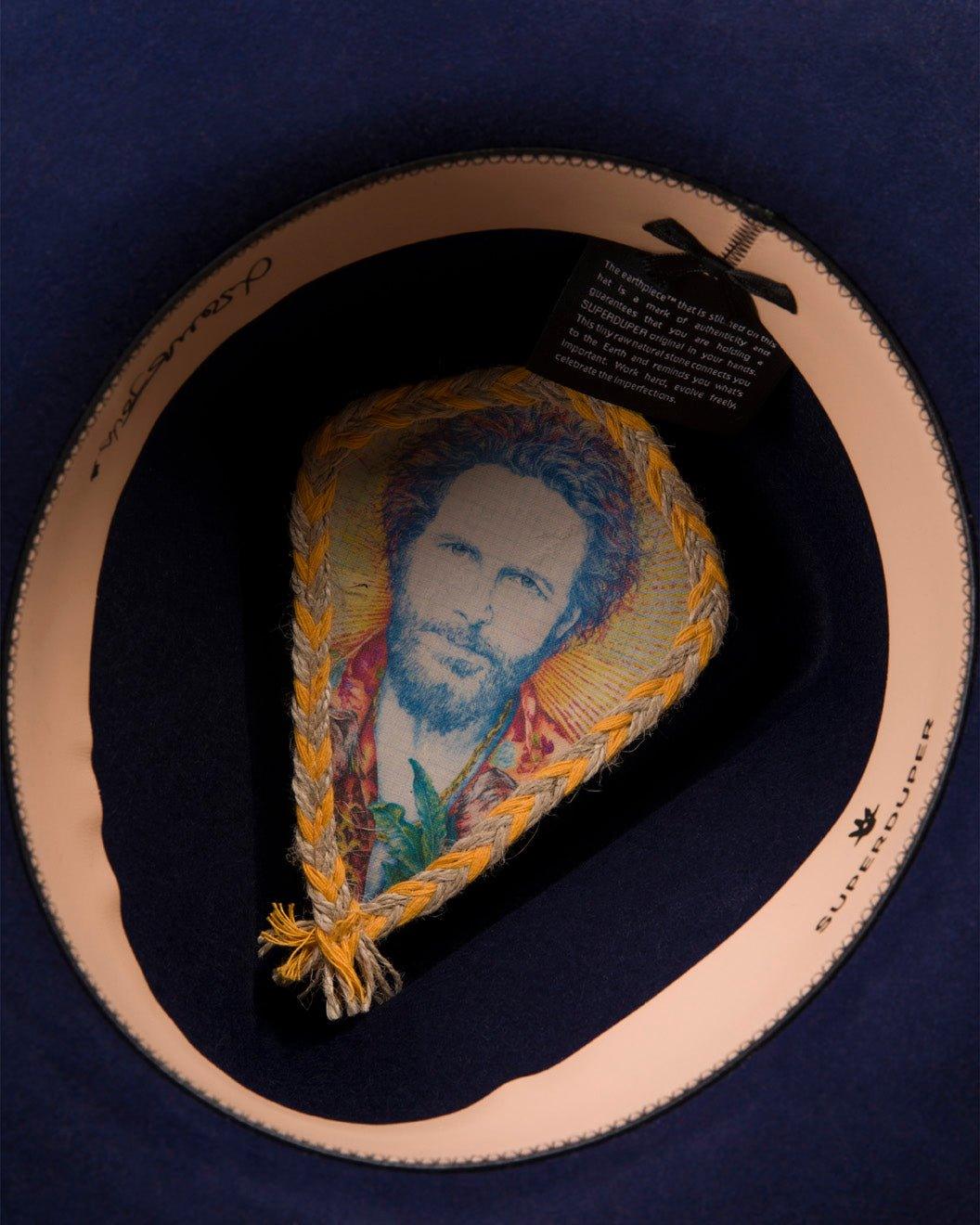 Interior of a wide-brim cobalt felt hat featuring a colorful patch with a bearded man's portrait.