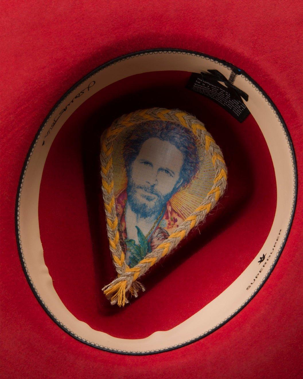 Inside view of a red felt Italian hat with braided detail and artistic portrait print on lining