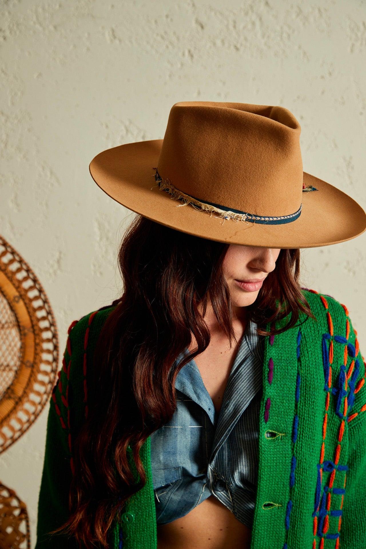 Woman wearing camel felt wide-brim hat with frayed band, green knit cardigan, and blue shirt