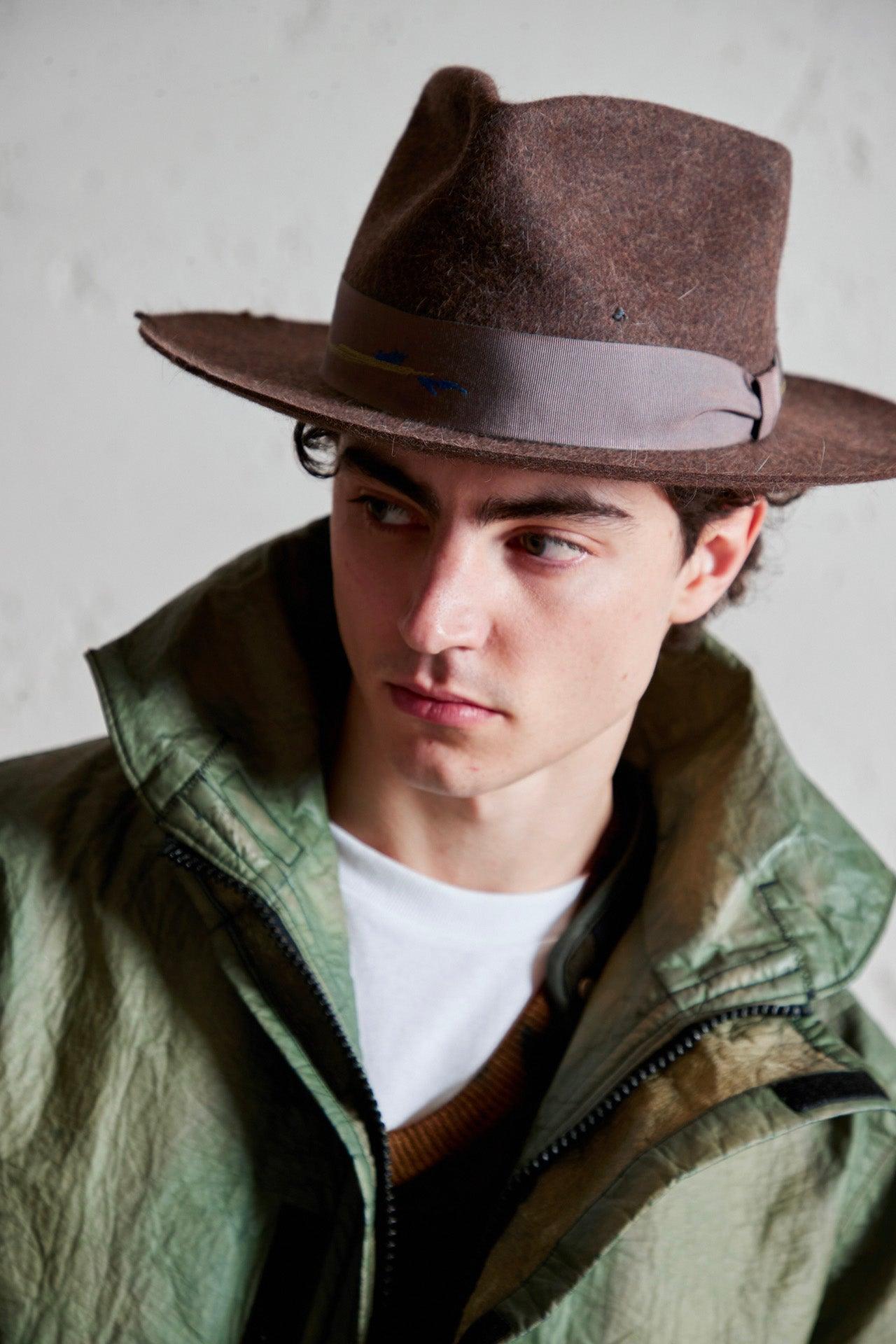 Man wearing a brown felt fedora hat with a gray ribbon, dressed in a green jacket.