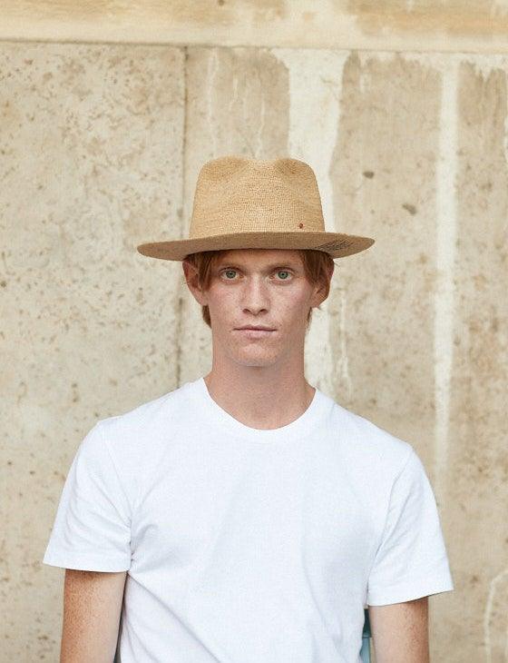 Man in a white t-shirt wearing a natural straw hat against a stone background
