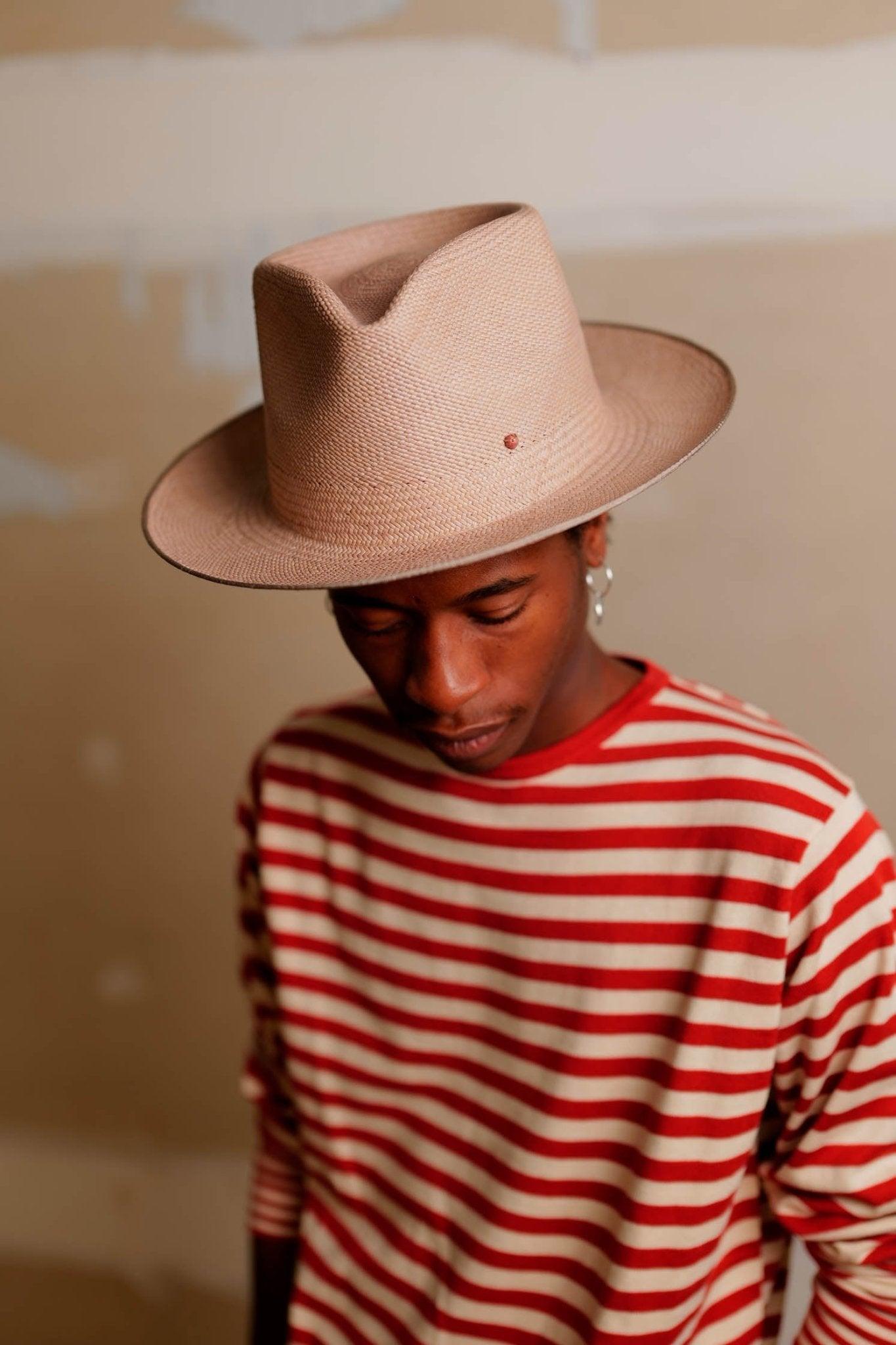 Man in a beige Panama hat and red striped shirt against a neutral background