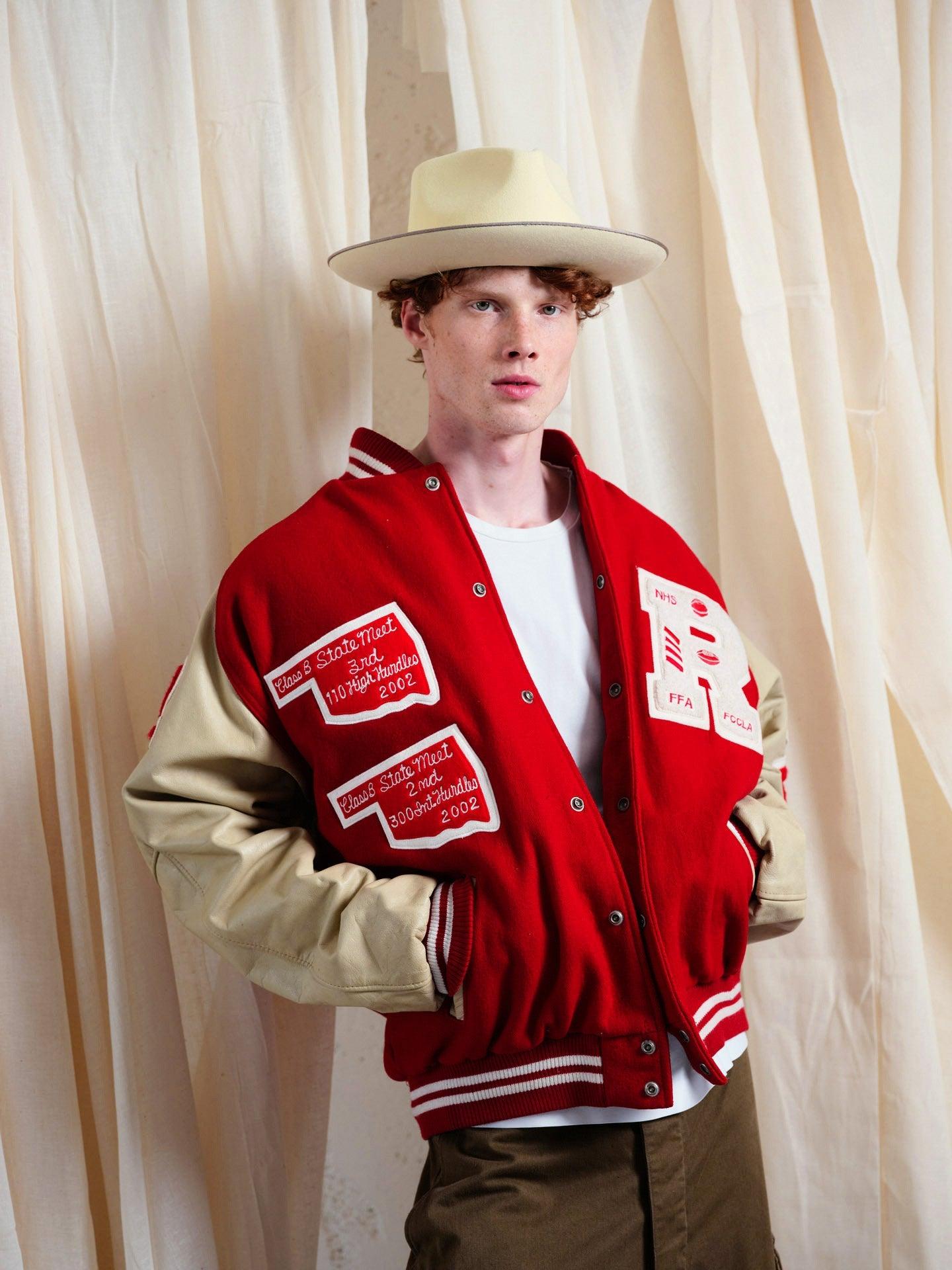 Man wearing handmade ivory felt wide-brim hat and red varsity jacket, cream backdrop