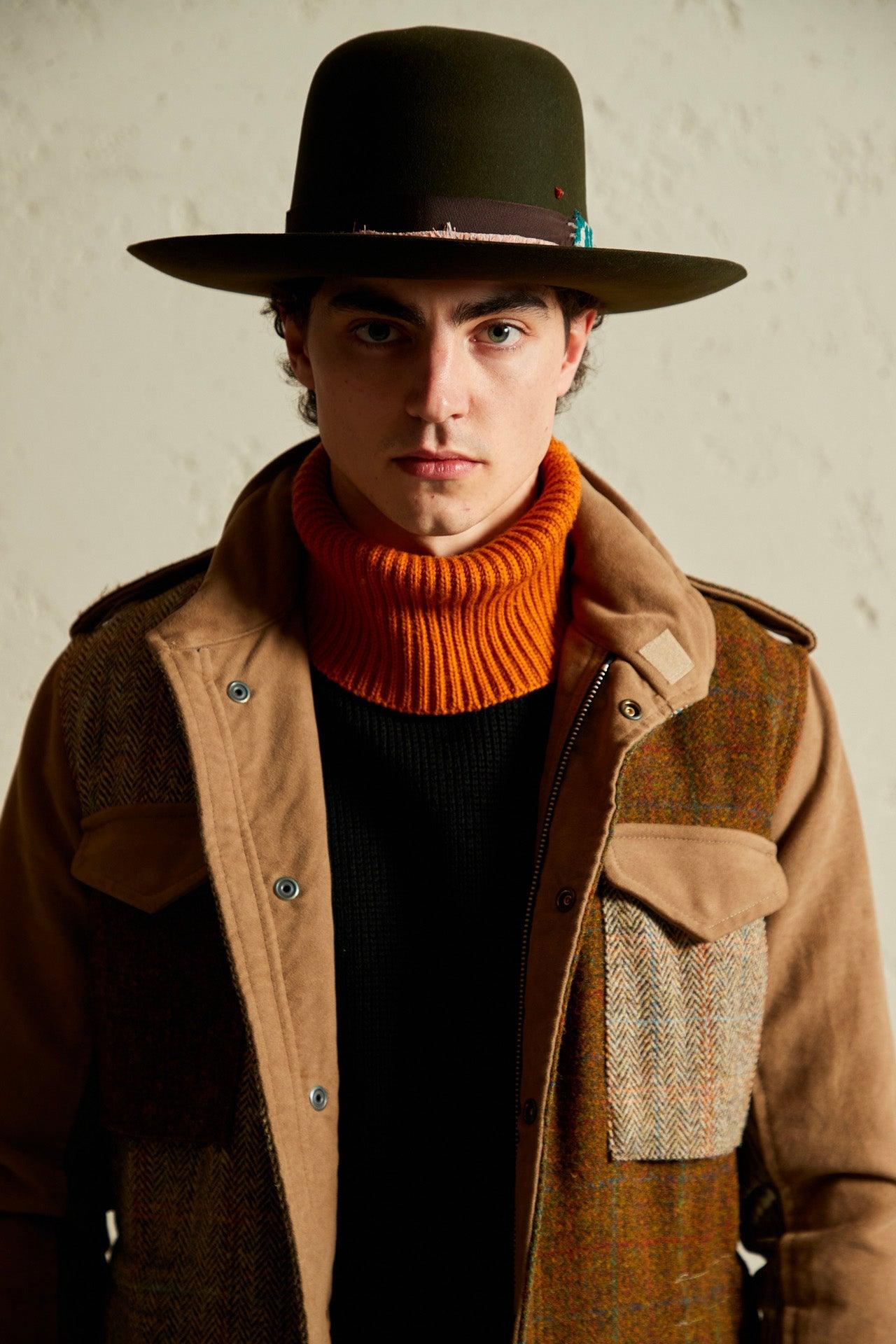 Man wearing olive green felt hat with wide brim, orange turtleneck, and brown patchwork jacket