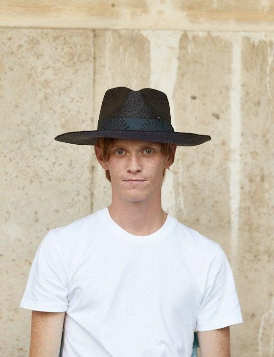 Man wearing a black wide-brimmed felt hat and white t-shirt against stone wall background