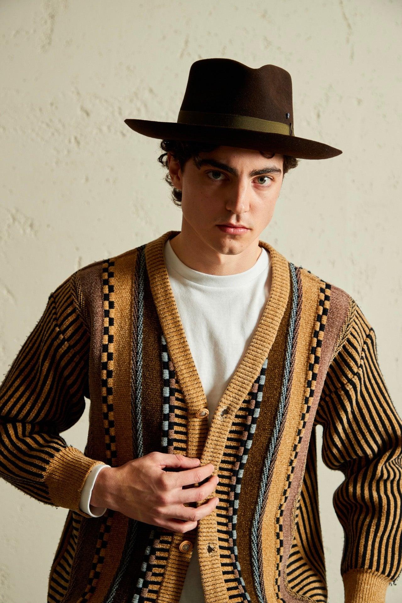 Man wearing a brown felt hat and a striped, patterned knit cardigan