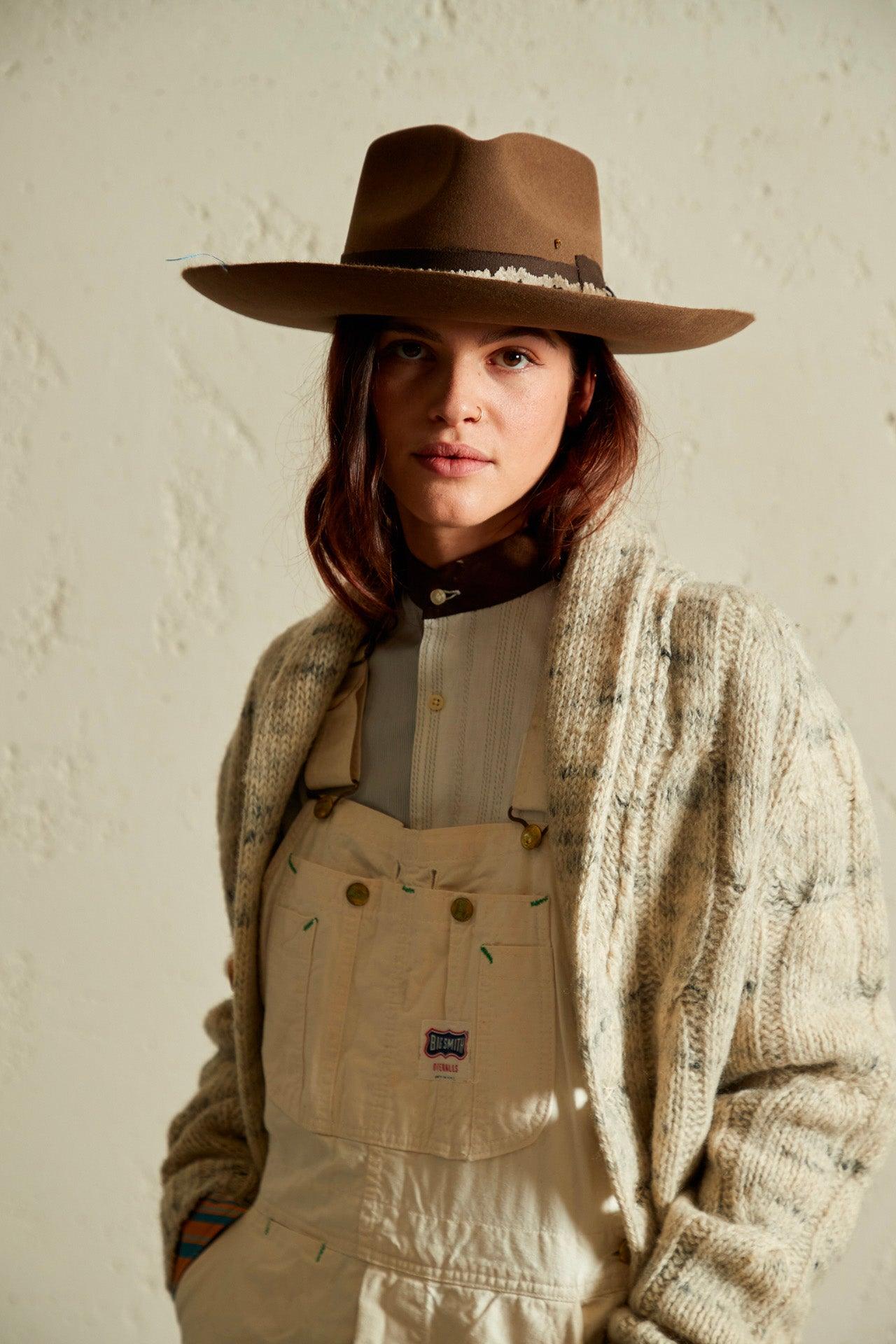 Woman wearing brown wide-brim felt hat and cream knit cardigan, neutral background