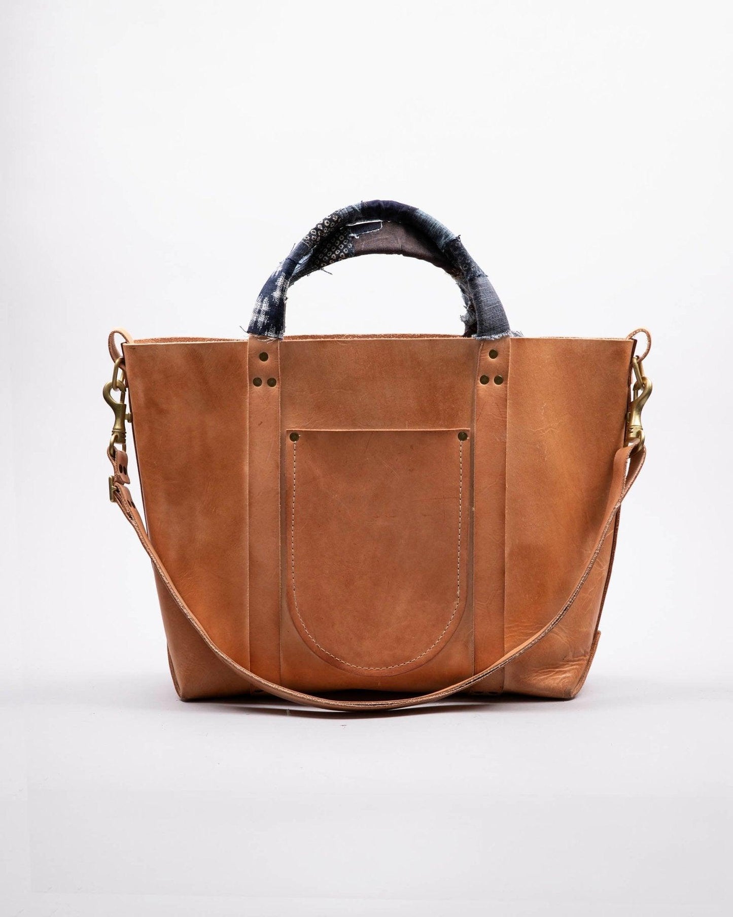 Tan leather tote bag with front pocket, detachable strap, and denim-wrapped handles